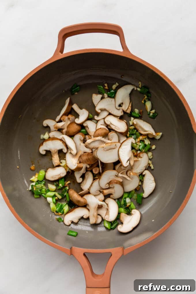Wok-Tossed Ho Fun 5 Fragrant green onions, garlic, and shiitake mushrooms sautéing together in a wok, releasing their delicious aromas.
