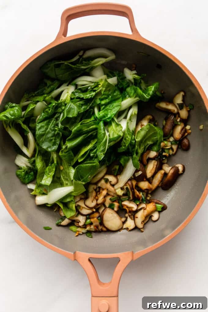 Wok-Tossed Ho Fun 6 Shiitake mushrooms and tender bok choy stir-frying in a vibrant pink pan, softening beautifully.