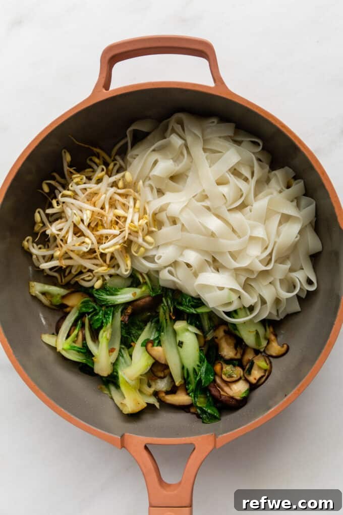 Wok-Tossed Ho Fun 7 A mix of colorful vegetables, including bok choy and mushrooms, combined with wide rice noodles in a pan, ready for sauce.