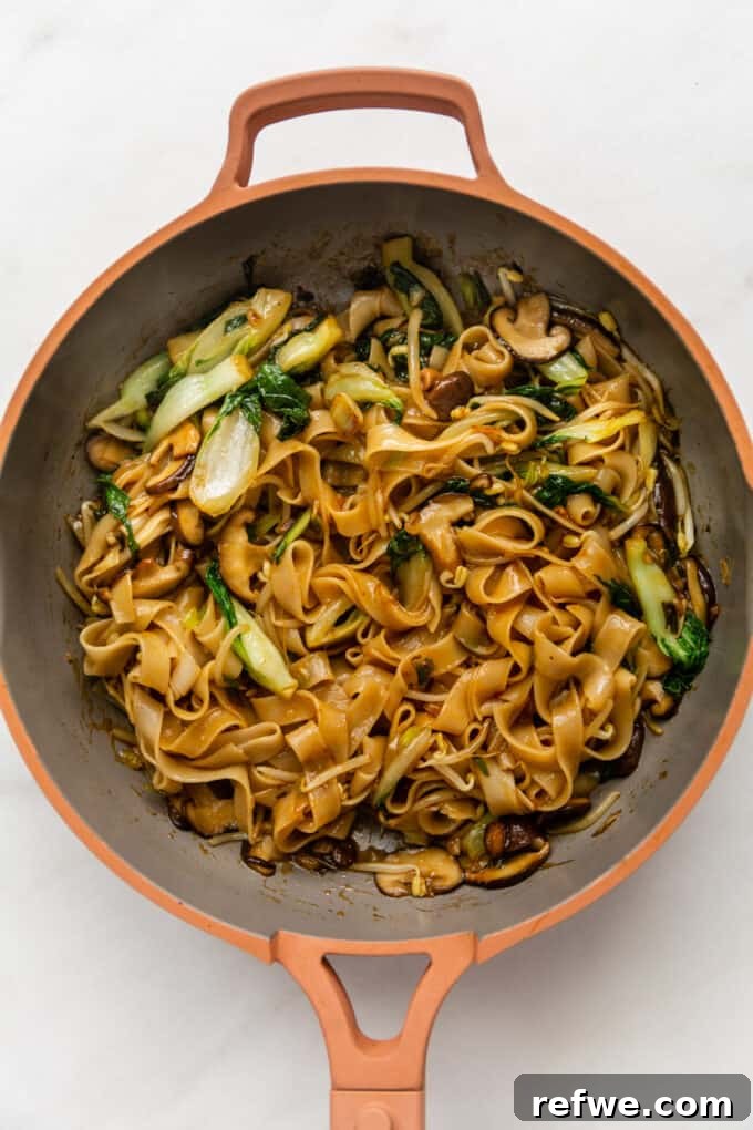Wok-Tossed Ho Fun 9 Perfectly stir-fried Ho Fun Noodles glistening with sauce and mixed with vegetables in a pink pan, ready to serve.