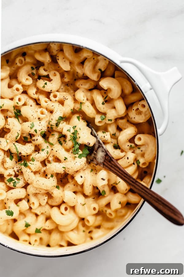 A large white pot brimming with vegan butternut squash mac and cheese, lightly seasoned with fresh pepper and chopped parsley, ready for serving.