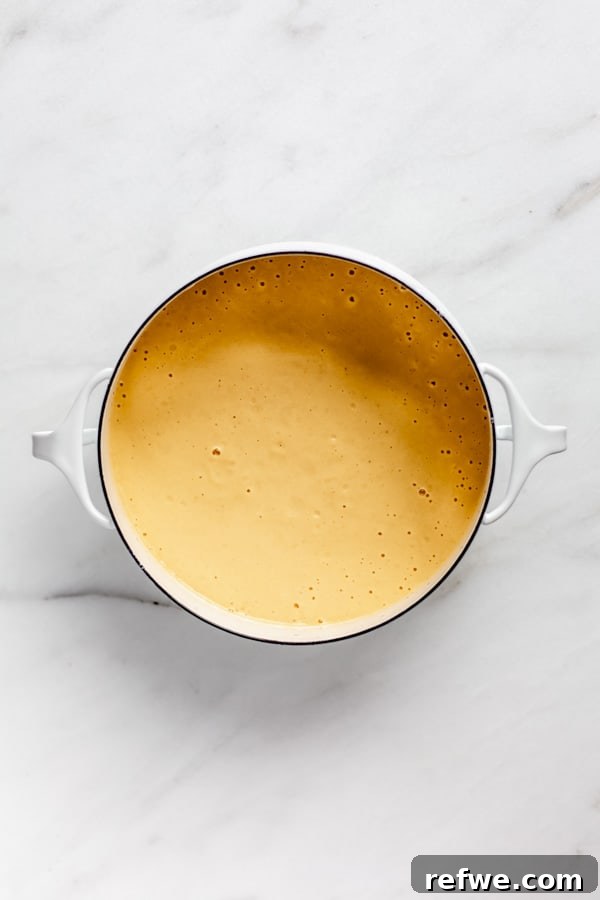 A white pot filled with the vibrant, creamy vegan butternut squash cheese sauce, ready for the pasta.