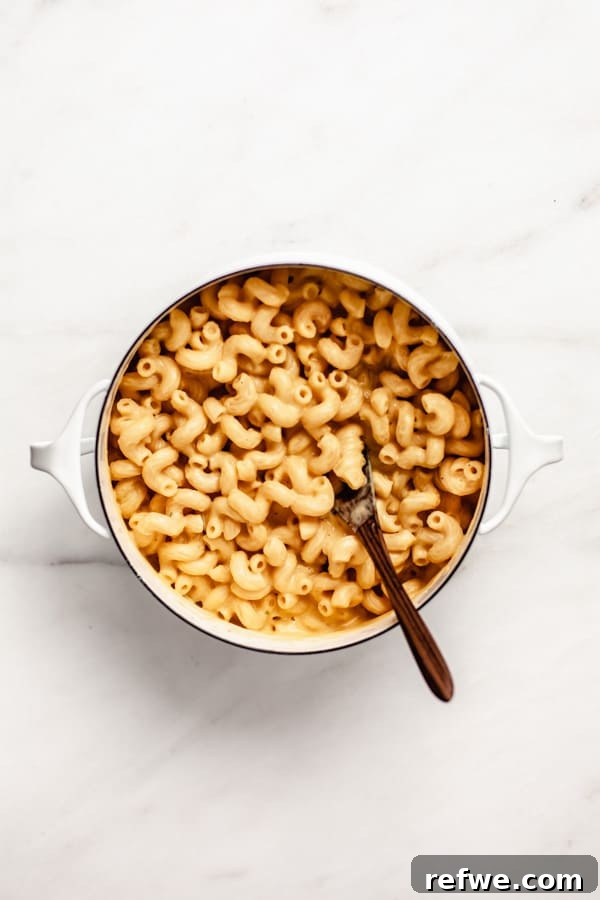 A white pot filled with perfectly combined butternut squash mac and cheese, a wooden spoon resting inside, ready to be served.