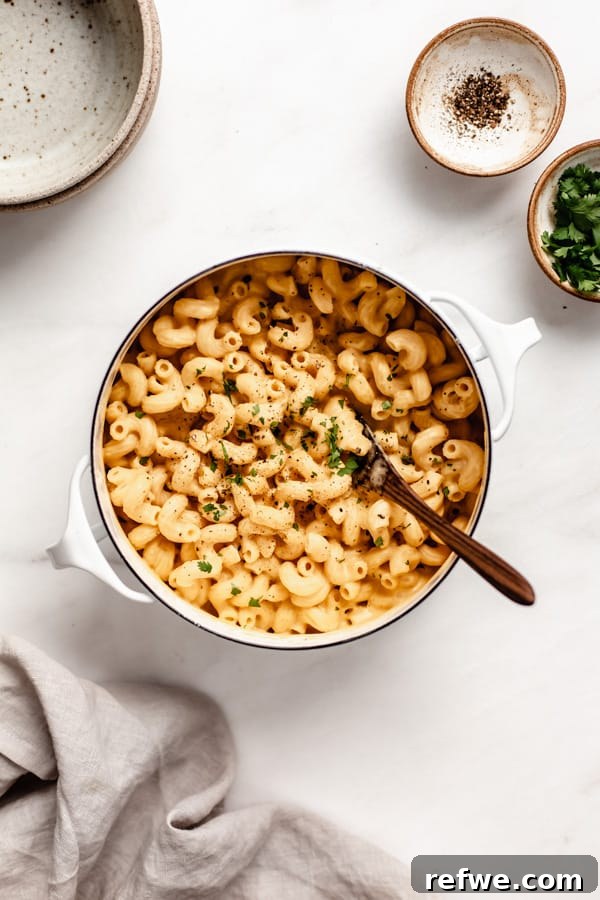 A pot of rich butternut squash mac and cheese, with small decorative bowls of fresh parsley and black pepper on the side, inviting you to customize your serving.