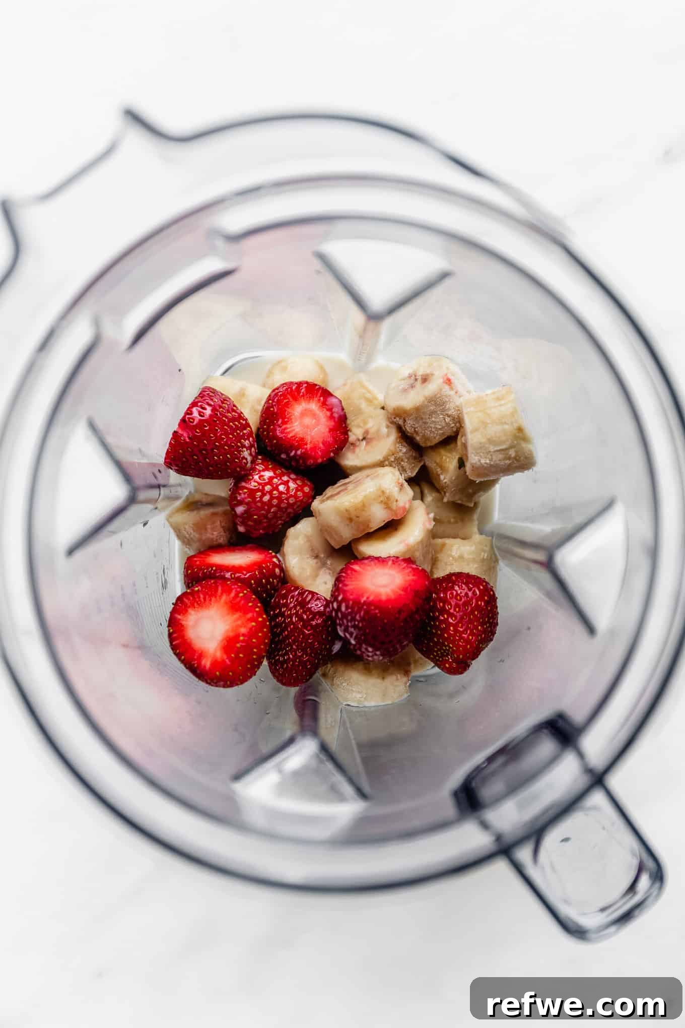 Strawberry Bliss Bowl 4 Fresh strawberries and sliced frozen bananas ready to be blended in a high-speed blender, capturing the first step of creating a vibrant smoothie bowl.