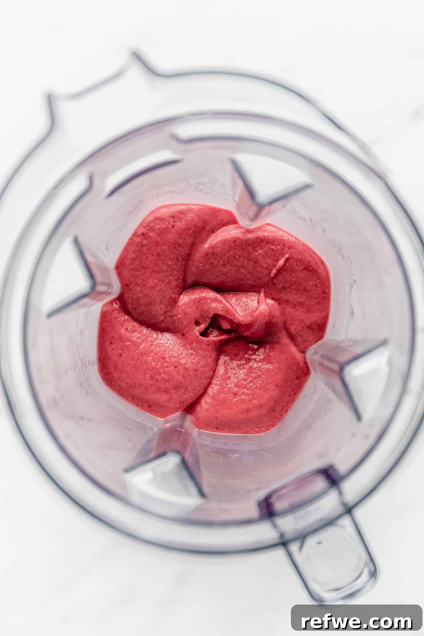 Strawberry Bliss Bowl 5 A high-speed blender actively blending the strawberry and banana mixture into a smooth, thick, and vibrant pink smoothie, illustrating the blending process.