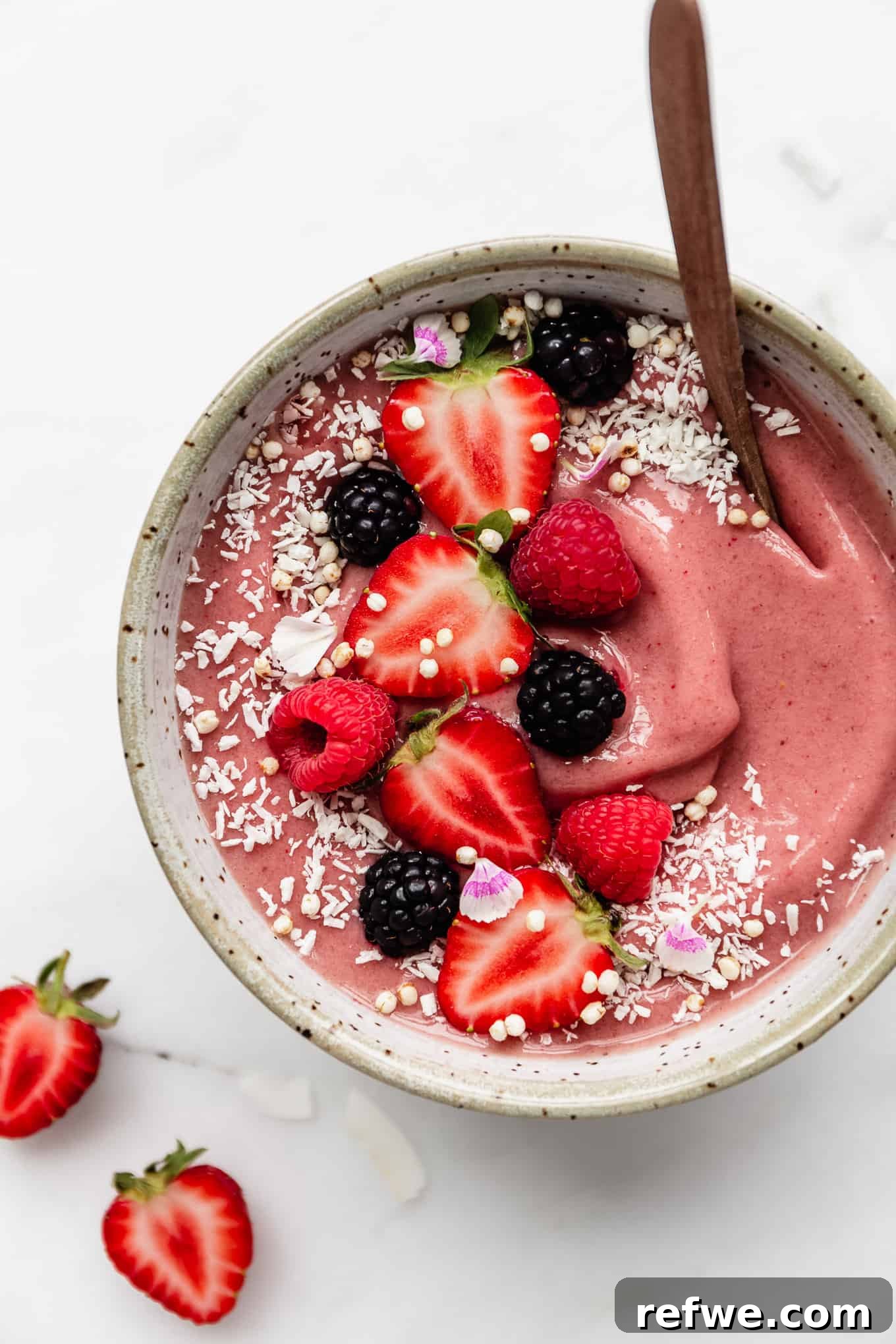 Strawberry Bliss Bowl 6 A beautifully prepared strawberry smoothie bowl, topped with a colorful array of fresh strawberries and a sprinkle of shredded coconut, presented in a white speckled bowl.
