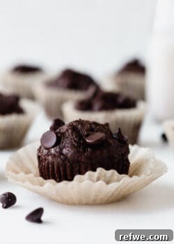 A healthy chocolate zucchini muffin in a paper liner, showcasing its rich brown color and speckled texture.