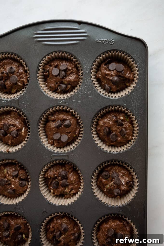 Wholesome Cocoa Zucchini Muffins 10 Unbaked chocolate zucchini muffins neatly arranged in a lined muffin pan, ready for the oven.