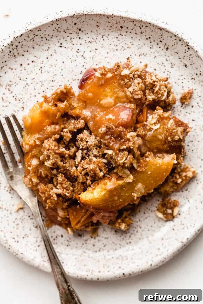 A slice of gluten-free peach crisp served on a white speckled plate with a fork, ready to be enjoyed.