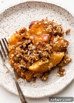 Gluten-Free Peach Crisp on a white speckled plate with a fork, ready to be eaten.