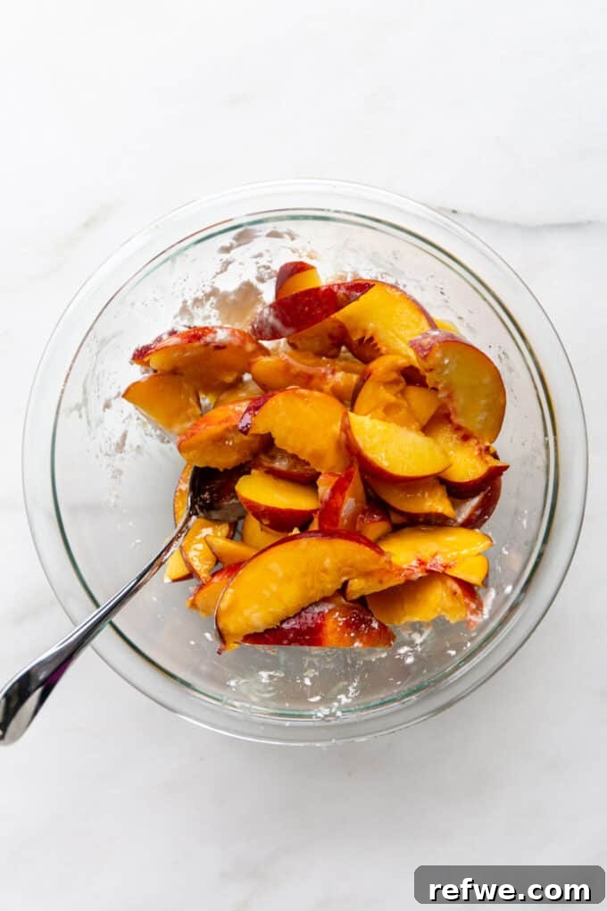 Peaches thoroughly tossed with cornstarch in a clear bowl, ready for the next step of the crisp recipe.