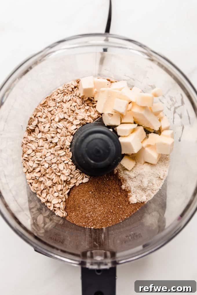 Cold butter cubes, rolled oats, coconut sugar, and almond flour in a food processor, ready to be pulsed into a crisp topping.