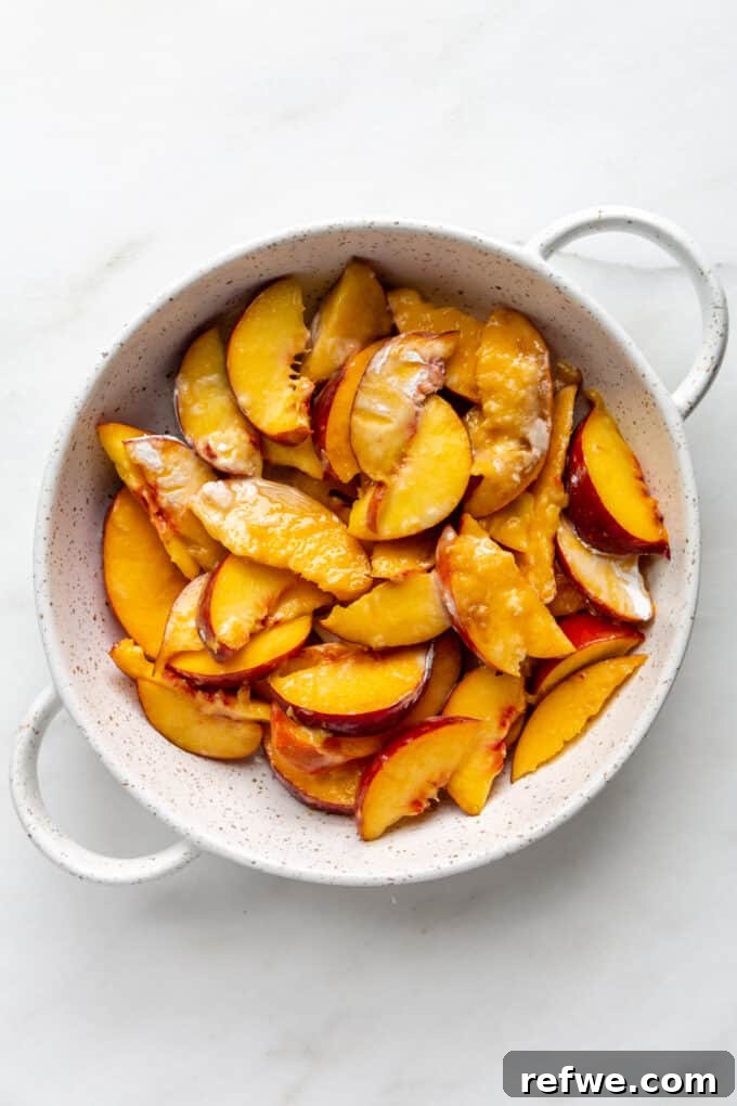 Peaches coated with cornstarch placed in a white baking dish, forming the base of the crisp.