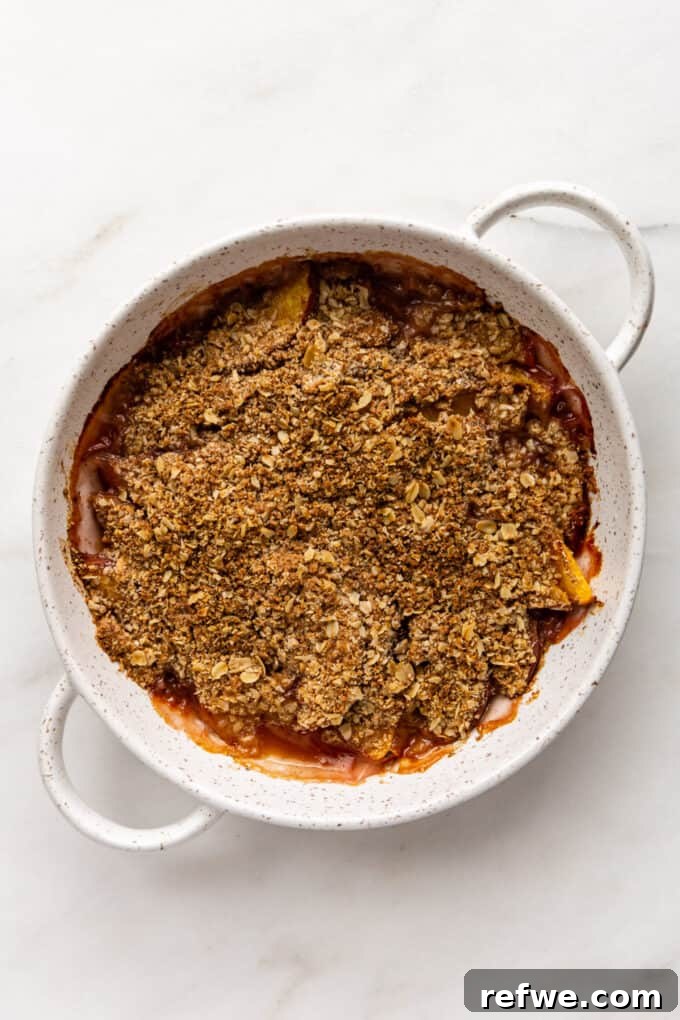 A freshly baked gluten-free peach crisp in a white speckled dish, with a perfectly golden and crispy topping.