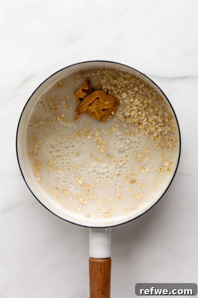 Nutty Oatmeal Delight 5 All the ingredients for peanut butter oatmeal – oats, almond milk, and peanut butter – simmering together in a white pot, being stirred.