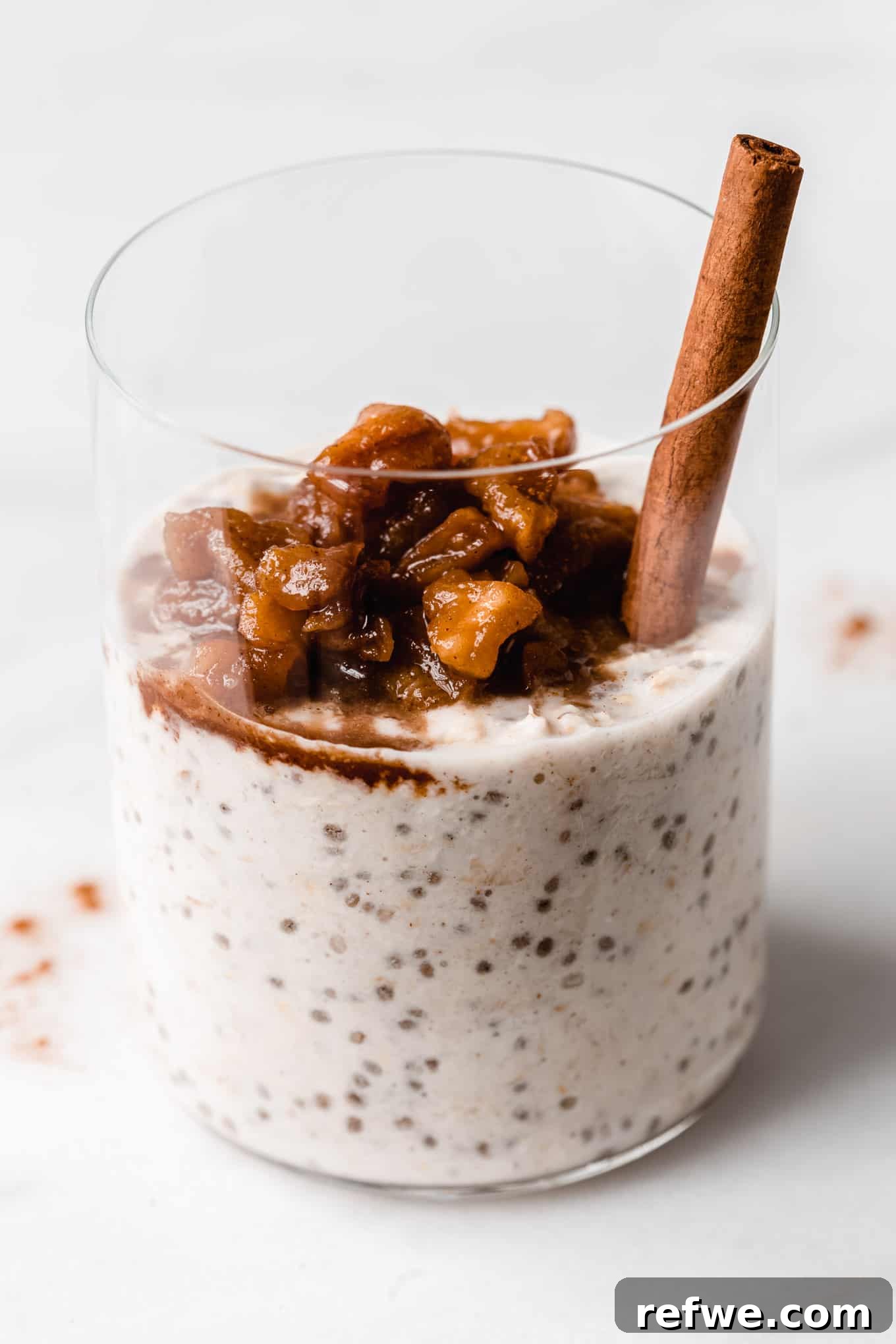 No-Bake Apple Pie Oats 11 A close-up shot of creamy overnight oats topped with warm, spiced stewed apples in a sleek white glass, showcasing its irresistible texture and appeal.