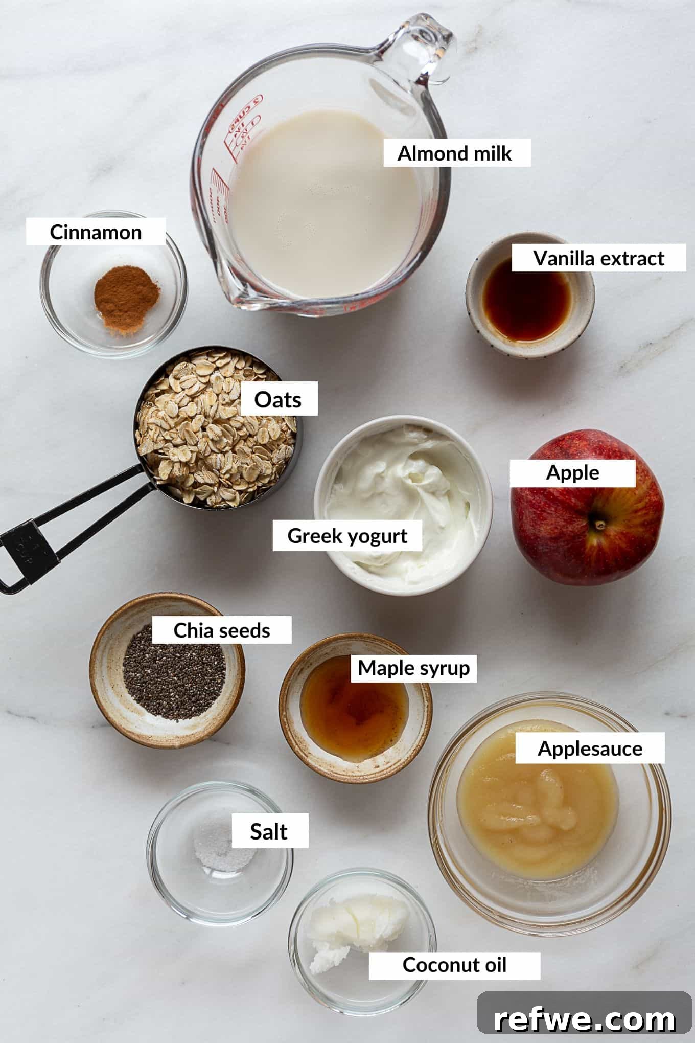 No-Bake Apple Pie Oats 3 A flat lay image showing all the essential ingredients needed to make apple pie overnight oats, including oats, chia seeds, apples, applesauce, and milk.