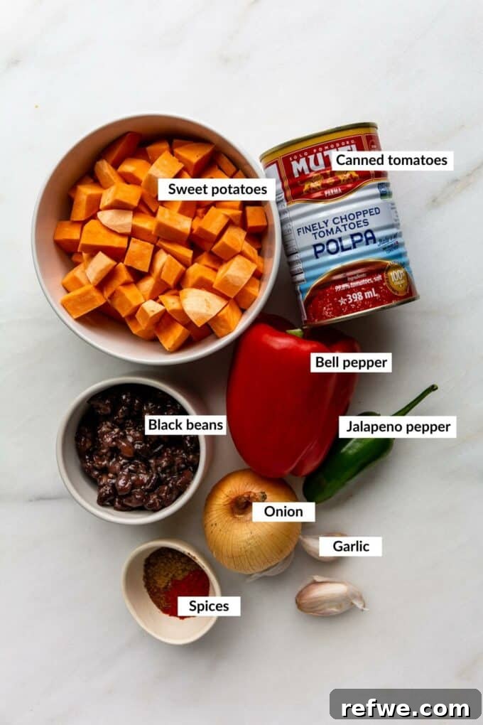 Hearty Sweet Potato Black Bean Chili 3 A flat lay of fresh vegetables including onions, garlic, bell peppers, jalapeños, and sweet potatoes, alongside cans of black beans and tomatoes, chili powder, smoked paprika, and cumin – all the ingredients for sweet potato chili.