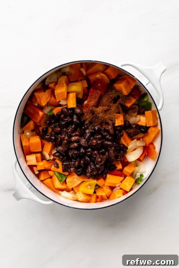 Hearty Sweet Potato Black Bean Chili 7 Black beans and spices mixed with the vegetables and sweet potatoes in a white pot.