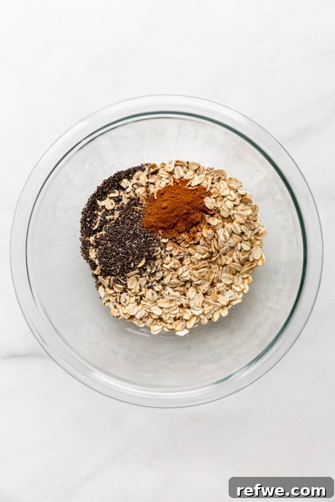 Overnight Autumn Pumpkin Delight 4 Dry ingredients like oats, chia seeds, and cinnamon in a clear mixing bowl, ready for combining.