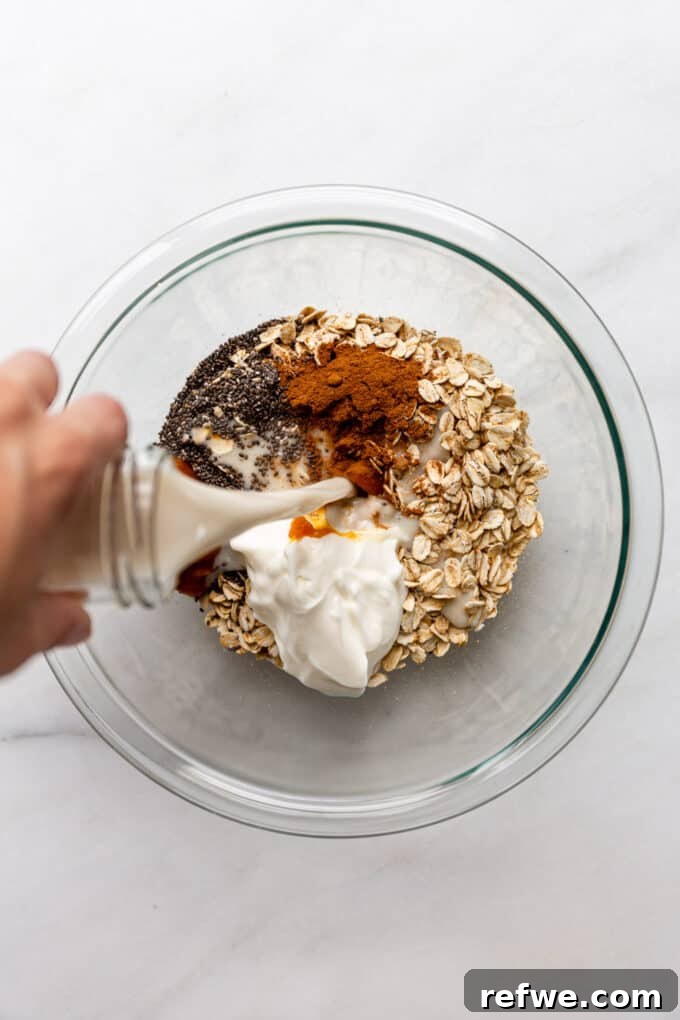 Overnight Autumn Pumpkin Delight 5 Almond milk being poured into a bowl of dry ingredients, pumpkin puree, yogurt, and other wet ingredients for overnight oats.