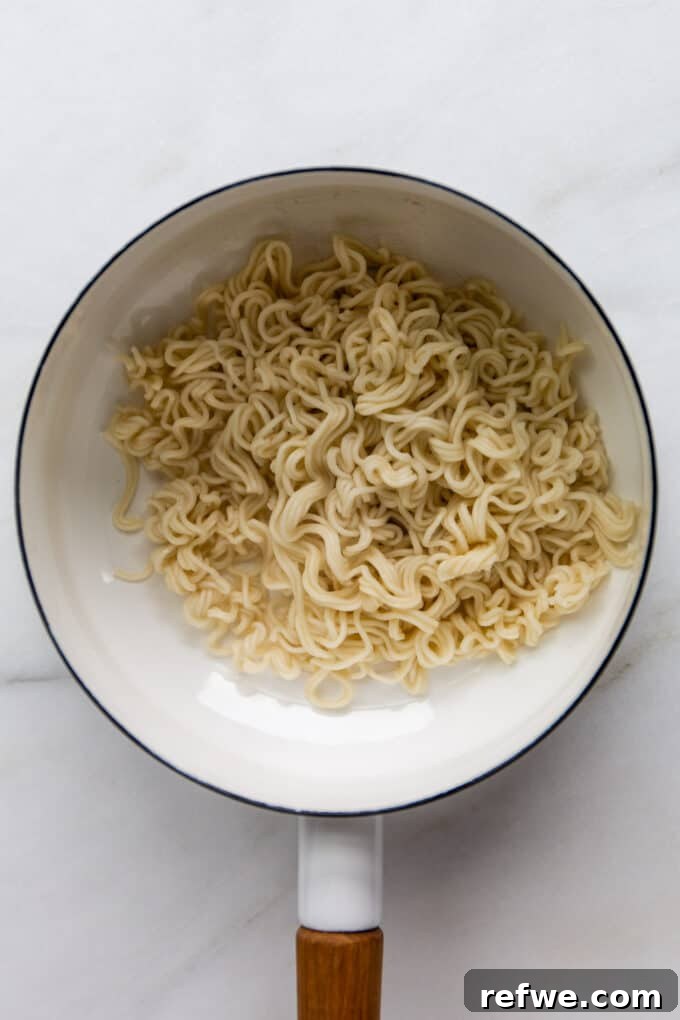 Cooked and drained ramen noodles resting in a white pot, ready to be coated with the flavorful sauce.