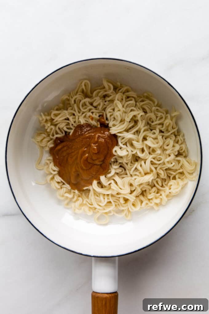 Ramen noodles and the creamy peanut butter sauce mingling in a white pot, just before being mixed together.