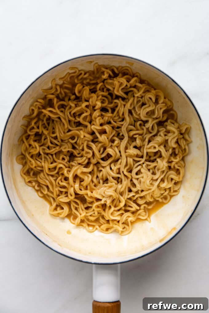 Creamy peanut ramen noodles evenly coated in sauce in a white pot, perfectly mixed and ready to be served.