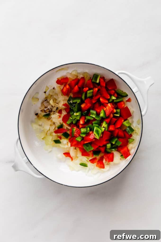 Sautéed bell peppers and jalapeños mixed with onions and garlic in a white pot, adding color and flavor to the chili base.