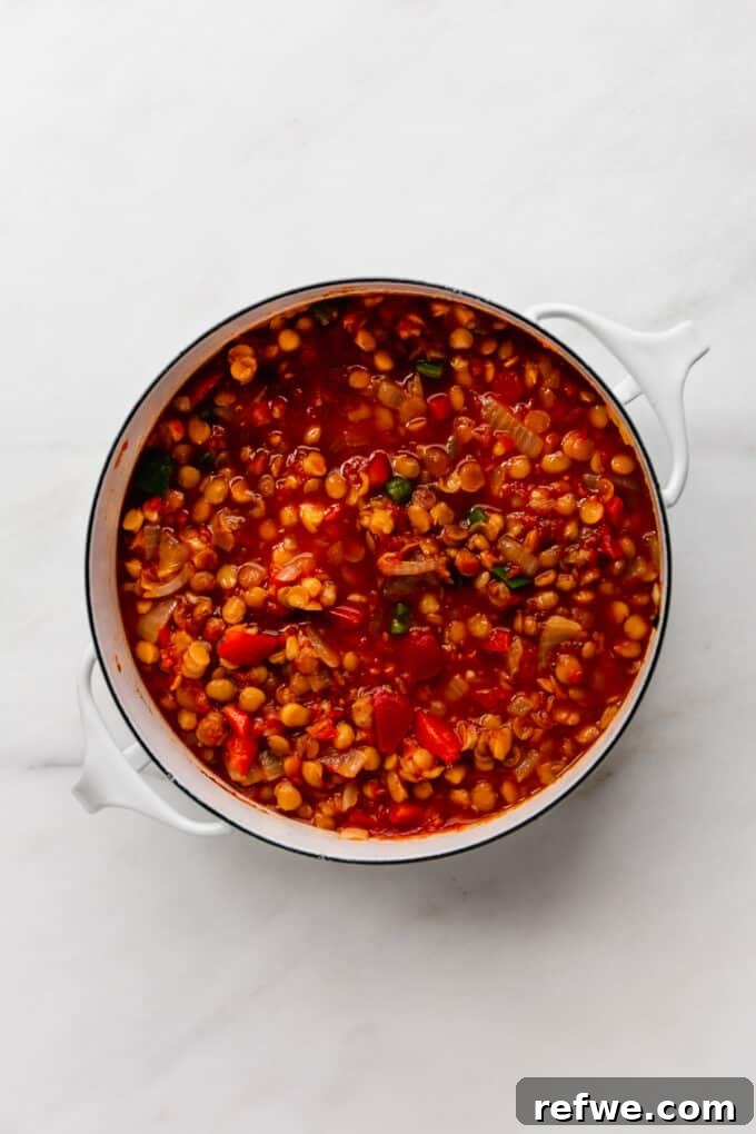 The lentil chili, now cooked and simmering in a tomato sauce with vegetables, showing a rich, thick consistency in the white pot.