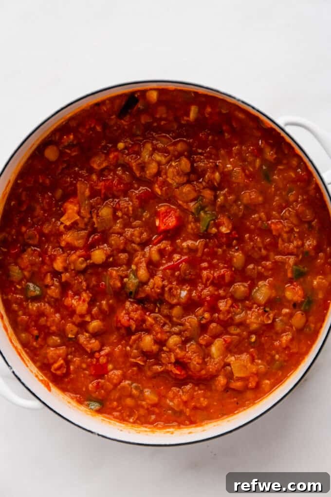 The fully cooked lentil chili resting in a white pot, ready to be served or optionally blended for a smoother texture.