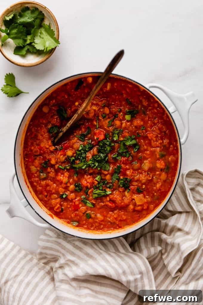 A large pot of hearty lentil chili, garnished with a beige striped napkin on the side, ready to be served.