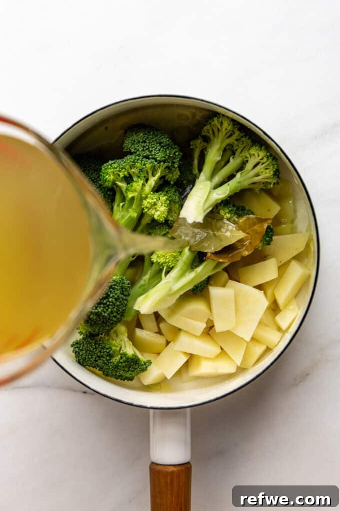 Wholesome Broccoli Potato Potage 6 A measuring cup pouring vegetable broth into a pot filled with broccoli, potatoes, and aromatics