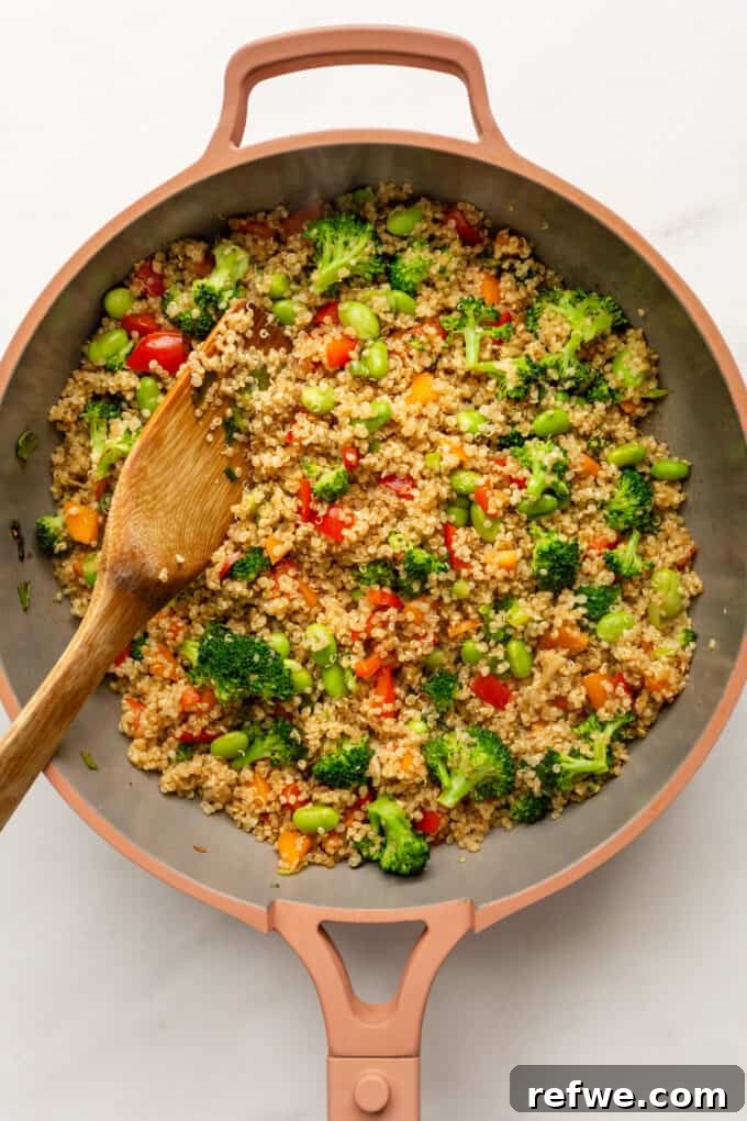 Wholesome Quinoa Stir-Fry 6 Finished Quinoa Fried Rice in a pink pan, stirred with a wooden spatula, ready to be served.