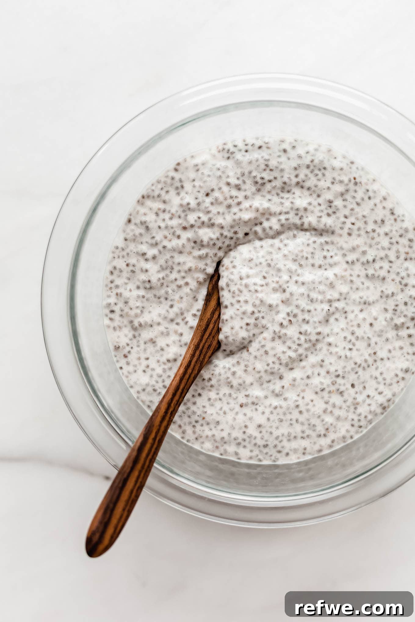 Apple chia pudding in a clear mixing bowl, showing its thick and creamy texture after setting.