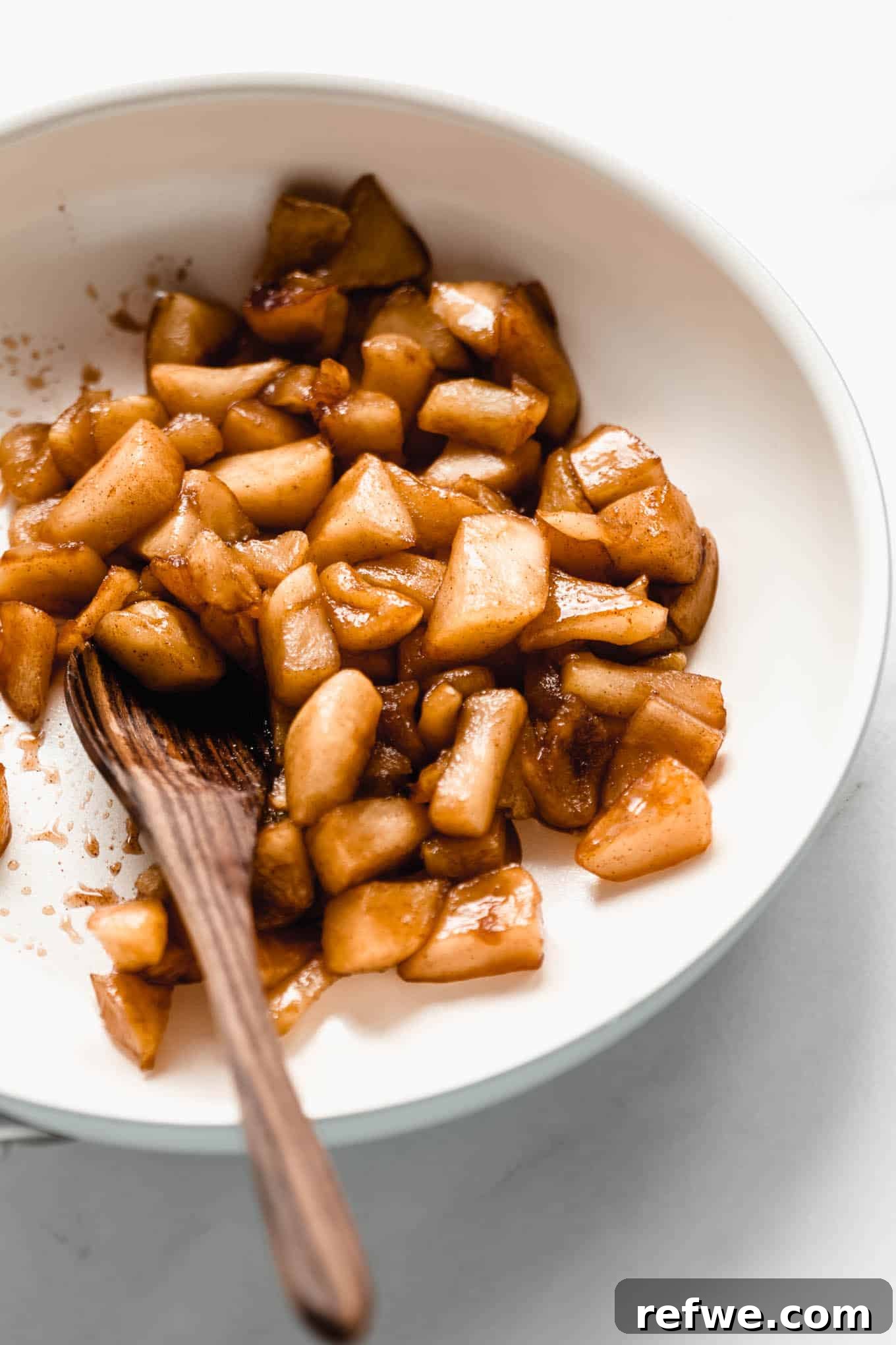 Glistening stewed apples simmering in a white pan, caramelizing beautifully.