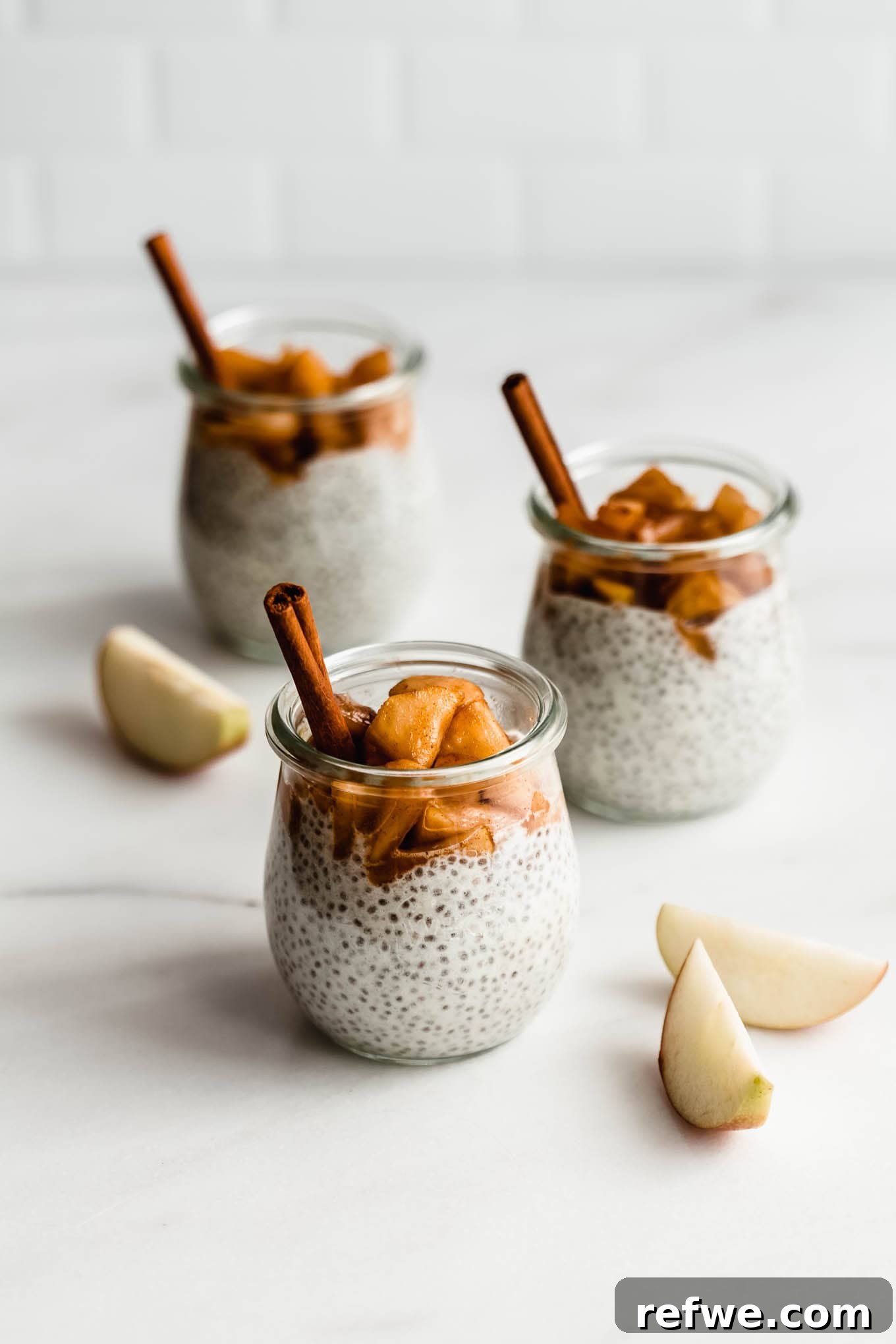 Three glass jars layered with creamy apple pie chia pudding and generous helpings of stewed apples.
