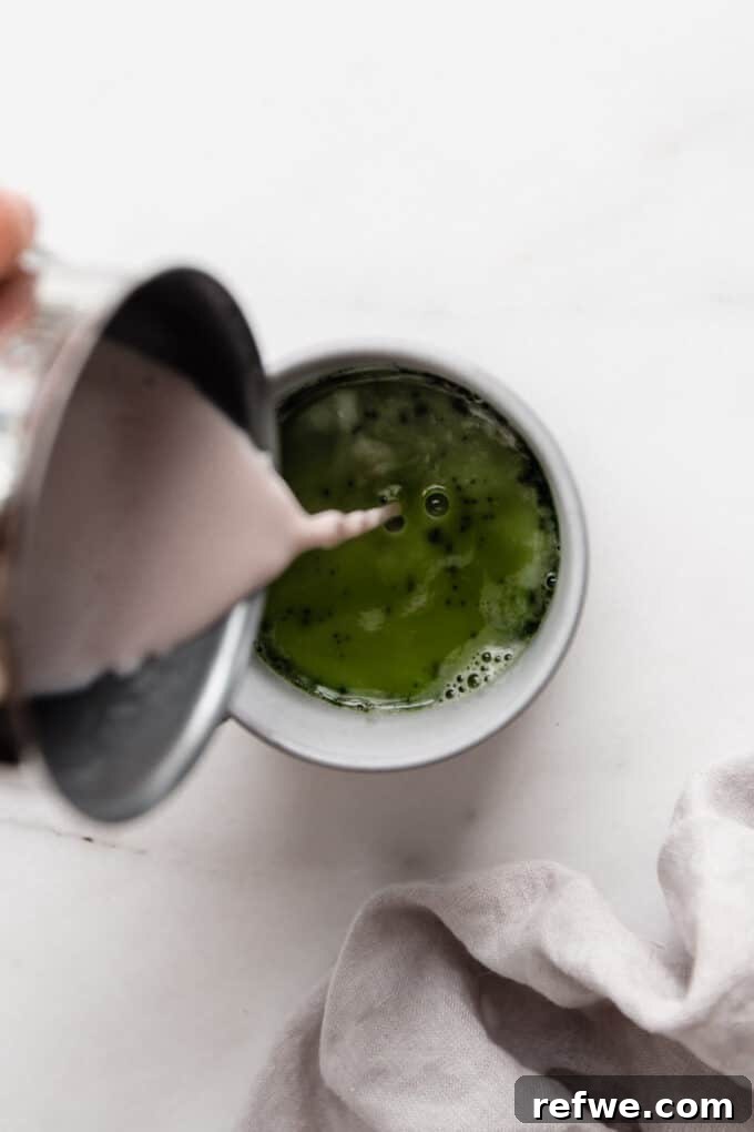 Frothed milk being poured into a mug containing whisked matcha tea.