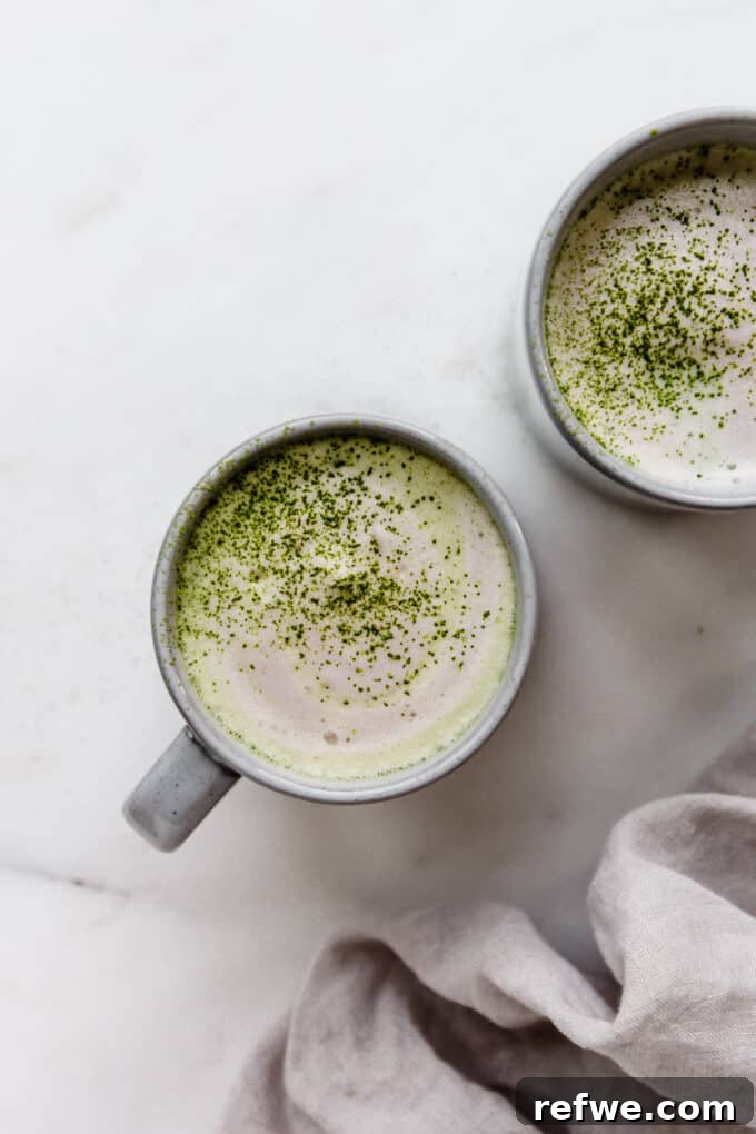 Two aesthetically pleasing mugs of matcha lattes, garnished with a sprinkle of matcha powder on top.