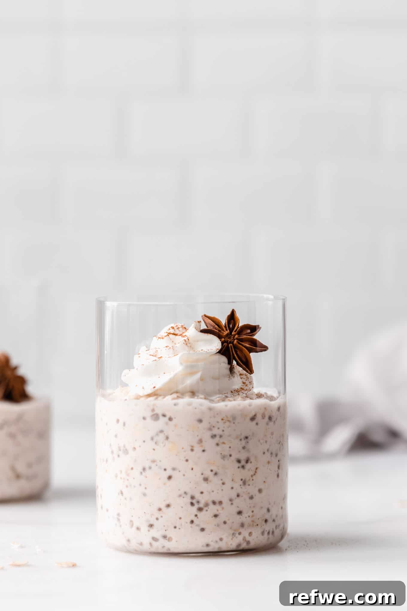 chai latte overnight oats in a cup topped with whipped cream and star anise