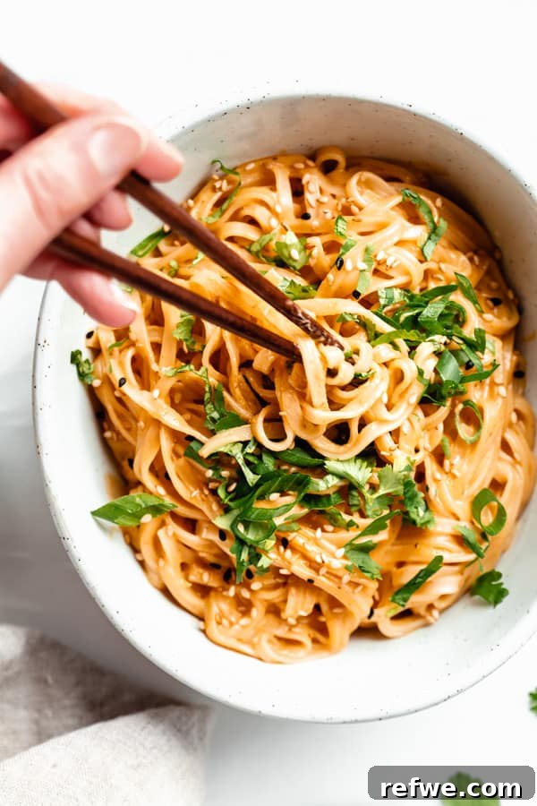 Spicy Thai Red Curry Noodles 13 A hand using chopsticks to pick up a bite of red curry noodles from a bowl, showing the creamy texture