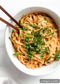 A bowl of red curry noodles topped with green onion and cilantro