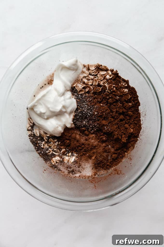Decadent Chocolate Overnight Oats 5 Yogurt and vanilla extract being added to the bowl of dry oat ingredients, ready for mixing.
