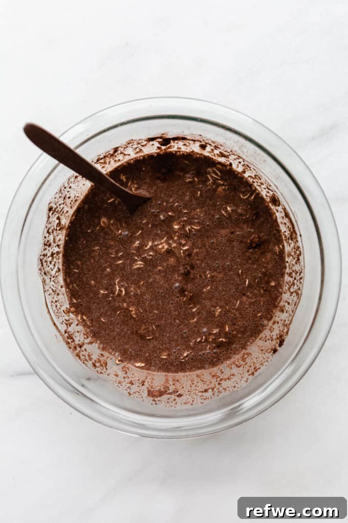 Decadent Chocolate Overnight Oats 6 Almond milk being poured into the mixture of oats, cocoa powder, chia seeds, and yogurt in a bowl.