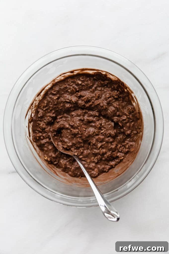 Decadent Chocolate Overnight Oats 7 A clear glass bowl filled with fully mixed chocolate overnight oats, covered with plastic wrap, ready for refrigeration.