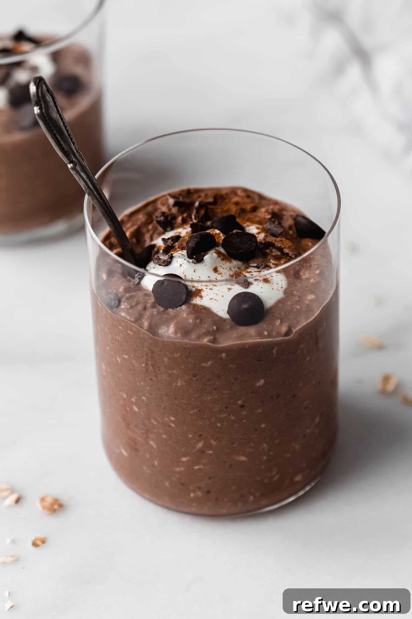 Decadent Chocolate Overnight Oats 8 A close-up shot of a cup of creamy chocolate overnight oats, garnished with fresh berries, with a spoon nestled inside.