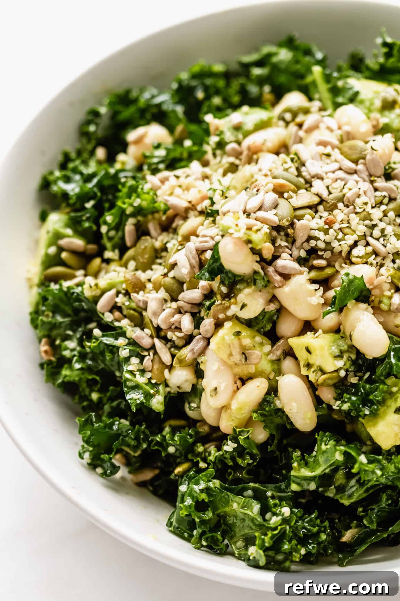 Hearty Kale and White Bean Power Bowl 2 Close up of a vibrant kale salad in a bowl, featuring creamy white beans, ripe avocado, and a sprinkle of wholesome seeds