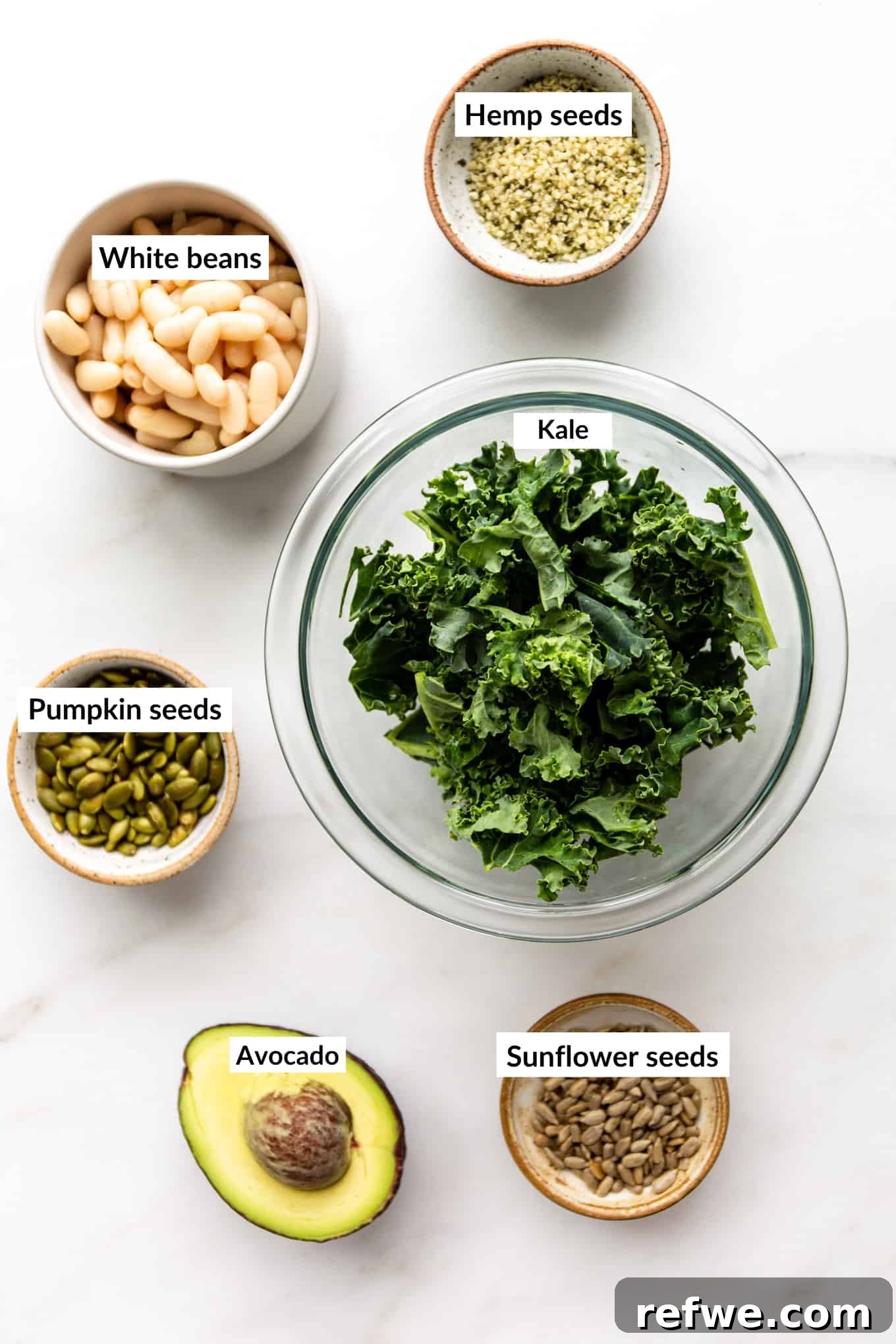 Hearty Kale and White Bean Power Bowl 3 A flat lay of fresh ingredients for kale white bean salad, including bunches of kale, a can of white beans, an avocado, and a mix of seeds
