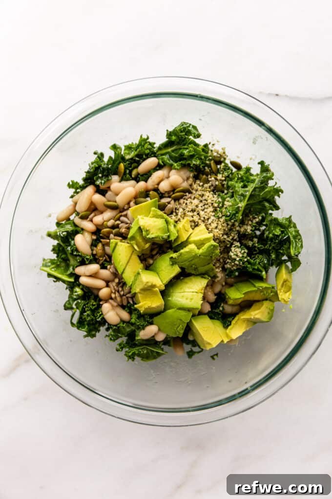 Hearty Kale and White Bean Power Bowl 5 Fresh kale, white beans, avocado cubes, and a mix of seeds in a clear mixing bowl, ready to be dressed